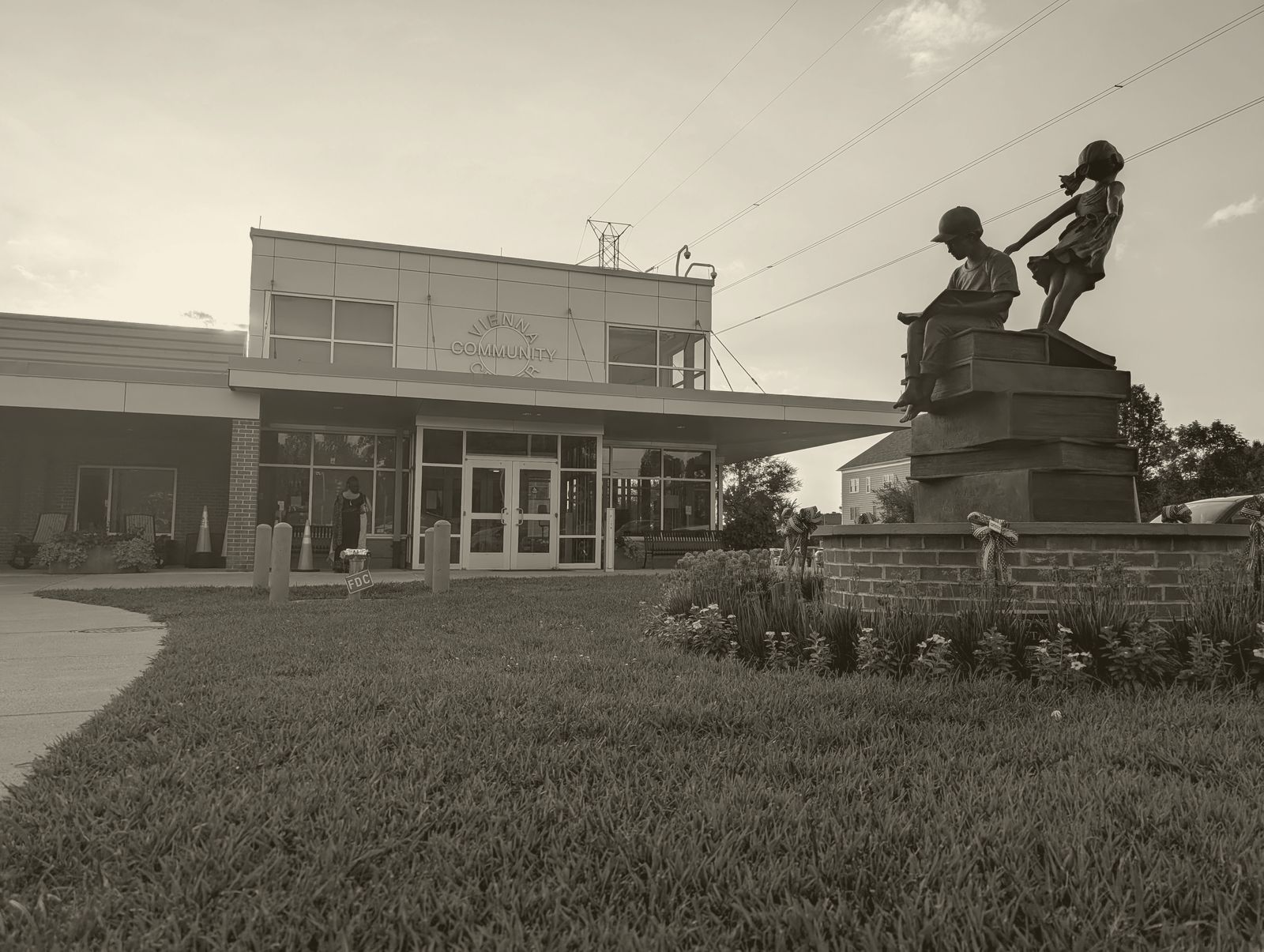 The Vienna Community Center entrance at dusk, beside a bronze statue of two children on a stack of books