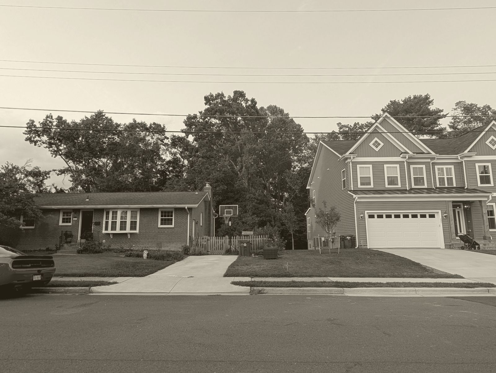 A one-story brick house next to a much larger newly built two-story house on the same street